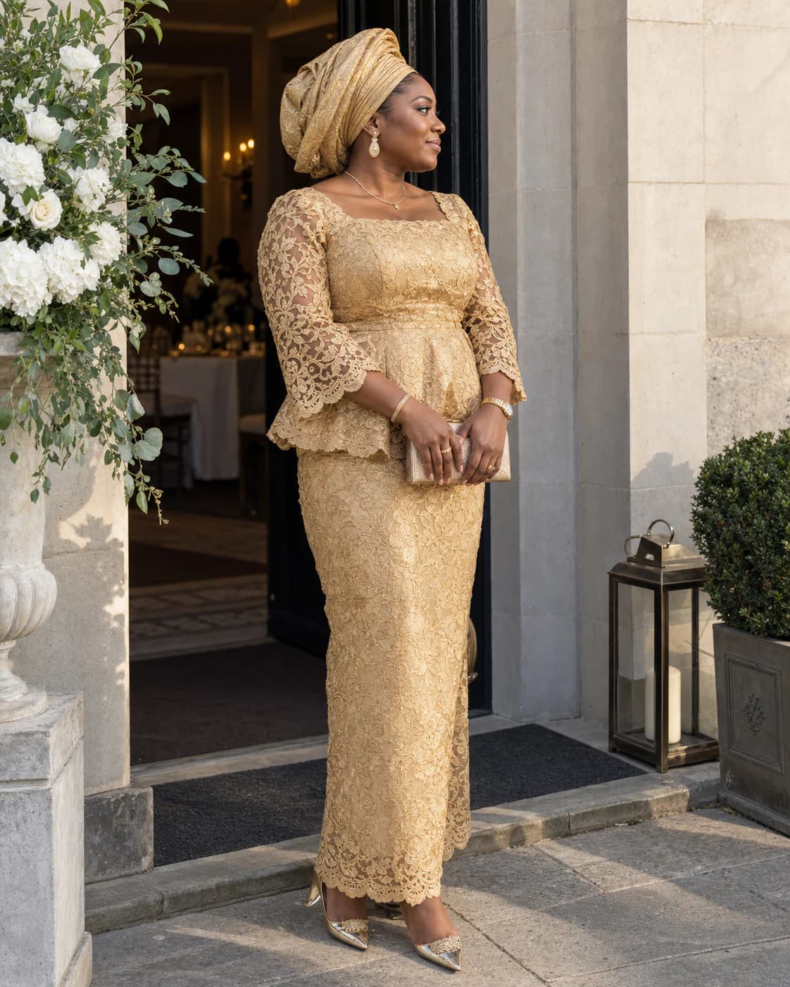 Woman in a gold corded-lace aso-ebi set and matching gele standing at the entrance of a wedding reception