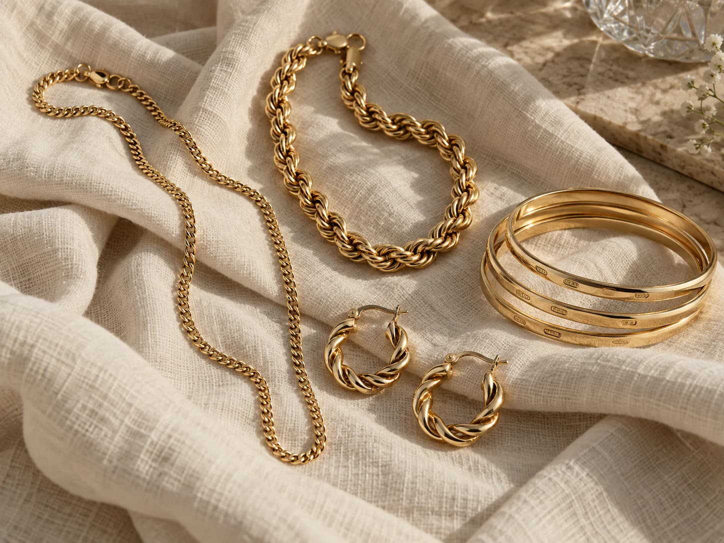 Layered gold chains and stacked bangles on a cream linen surface