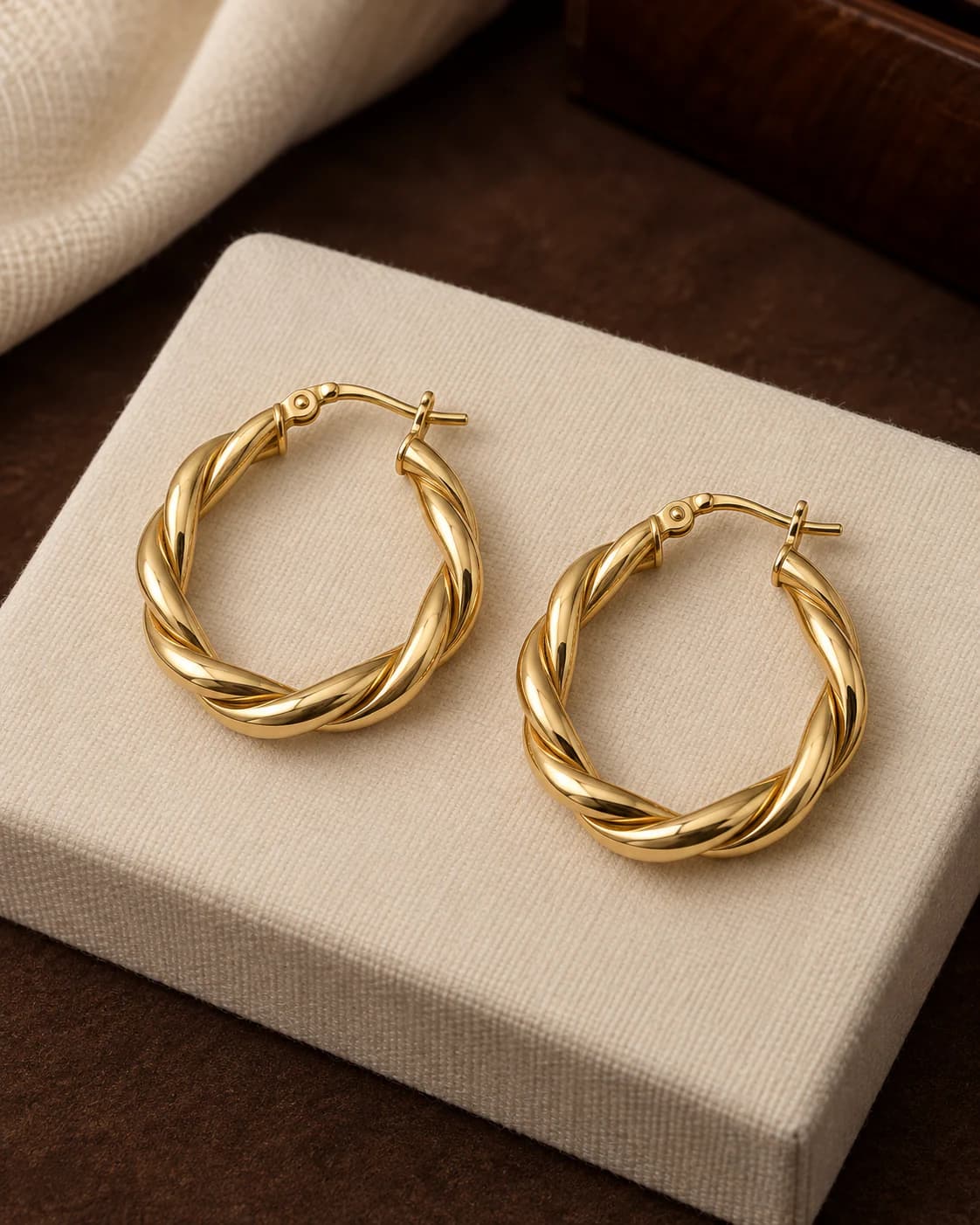 Twisted Hoop Earrings, 18ct in 18ct yellow gold, front view on a plain champagne background